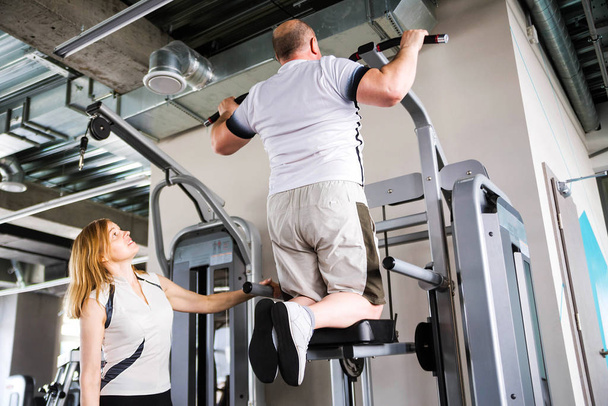 Older couple in the gym. Man doing pull-up exercise - 写真・画像