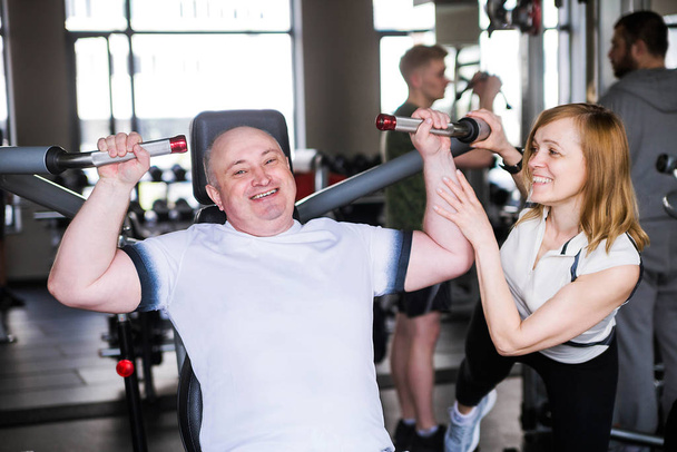 Couple plus âgé dans la salle de gym. Un homme fait un exercice sur ses bras et ses épaules
. - Photo, image