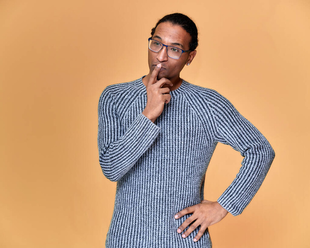 Portrait of a young African American man in glasses with a short haircut and with a white-toothed smile in a gray sweater on a pink background. Standing and talking right in front of the camera. - Foto, immagini