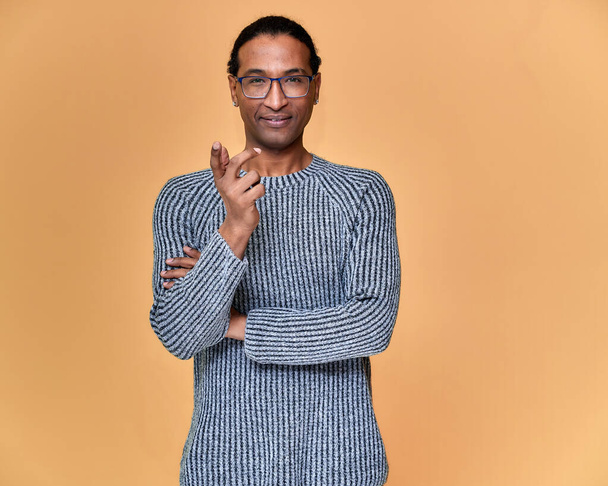 Portrait of a young African American man in glasses with a short haircut and with a white-toothed smile in a gray sweater on a pink background. Standing and talking right in front of the camera. - Valokuva, kuva