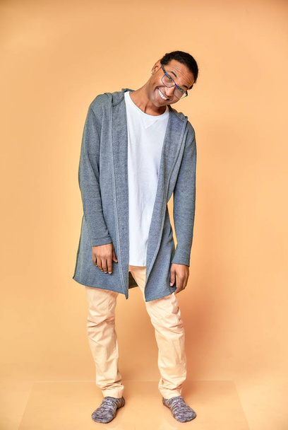 Vertical portrait of a cheerful young man wearing glasses African-American with a short haircut in ordinary clothes on a pink background in full length. Standing right in front of the camera - Foto, Imagen