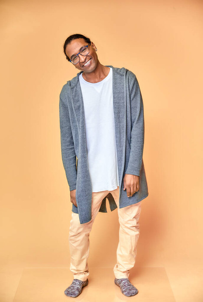 Vertical portrait of a cheerful young man wearing glasses African-American with a short haircut in ordinary clothes on a pink background in full length. Standing right in front of the camera - Foto, Imagem