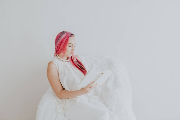 όμορφη γυναίκα με ροζ μαλλιά διαβάζοντας ένα βιβλίο σε ένα λευκό δωμάτιο - Φωτογραφία, εικόνα