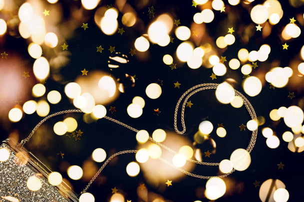 Feestelijke avond gouden koppeling met ster hagelslag op zwart. Vakantie en viering achtergrond. Luxe accessoires en feestconcept. Kerstmis en Nieuwjaar Feestdag met feestelijke bokeh lichten - Foto, afbeelding