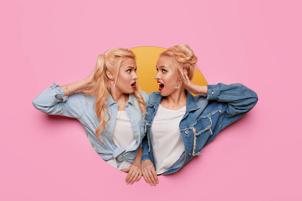 Image of two young happy shoked girlfriends women. Twins Peeping through a pink hole in the wall. Big Discount Season. Copy space for text - Fotó, kép