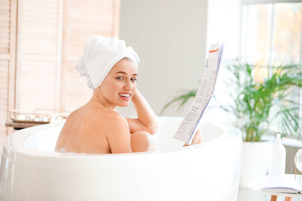 Mooie jonge vrouw die krant leest in de badkamer - Foto, afbeelding