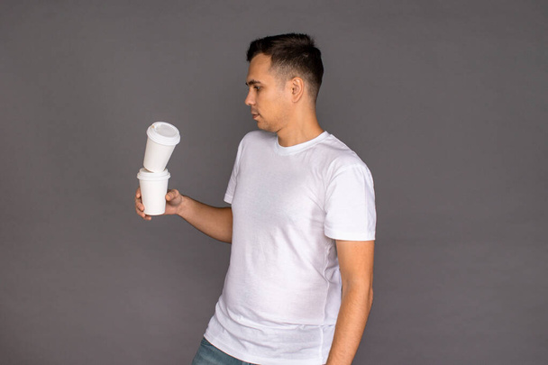 A guy in a white t-shirt juggles glasses of coffee, drops them on the ground. - Foto, Imagem