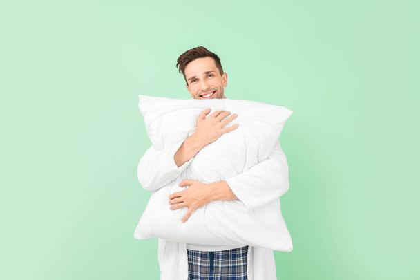 Όμορφος άντρας με μπουρνούζι και μαξιλάρι σε φόντο χρώματος - Φωτογραφία, εικόνα