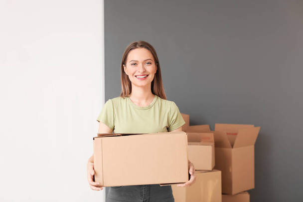 Happy young woman with moving box in new house - Foto, afbeelding