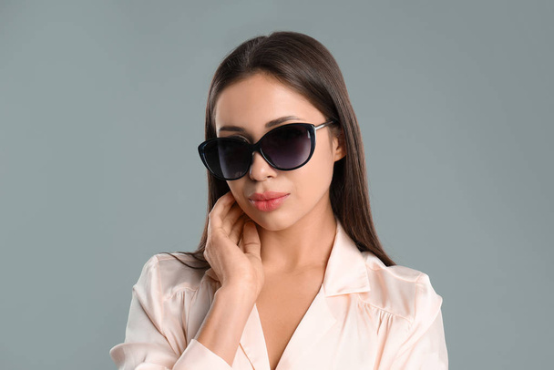 Beautiful young woman wearing sunglasses on grey background - Valokuva, kuva