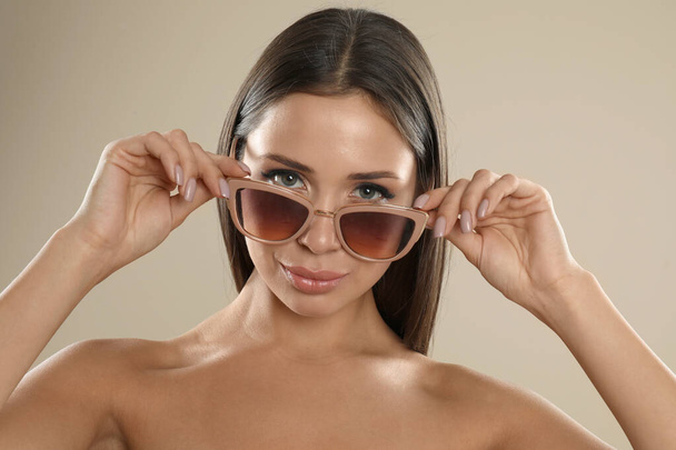 Beautiful young woman wearing sunglasses on beige background - Fotoğraf, Görsel