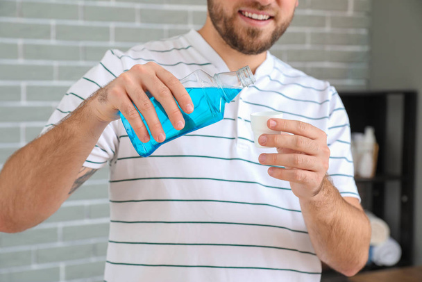 Handsome young man with mouth rinse in bathroom - Photo, Image