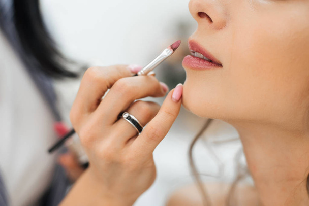 artista profissional faz maquiagem pinta lábios com uma escova com batom no rosto de uma jovem
 - Foto, Imagem