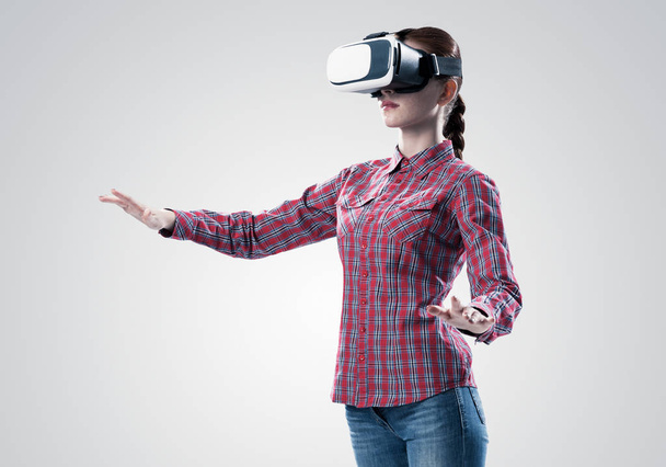 Young woman in checked shirt wearing virtual helmet against gray background - Foto, Imagen