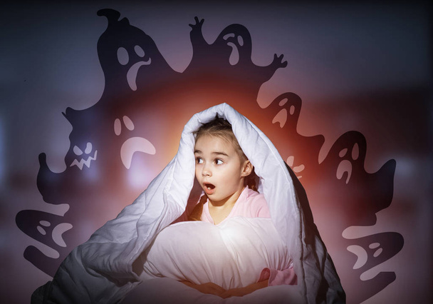 Excited girl hiding under blanket from imaginary ghosts. Scared kid sitting in his bed at home. Little girl afraid of fantasy monsters. Covered child in pajamas not sleep at night. Halloween holiday. - Photo, image