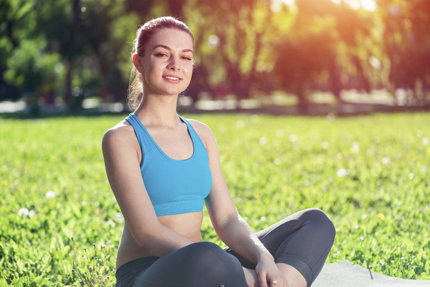 Girl meditates in lotus pose on green grass. Practicing of yoga at summer park. Portrait of young peaceful woman. Training and meditation outdoor at summer day. Healthy lifestyle and relaxation. - Zdjęcie, obraz