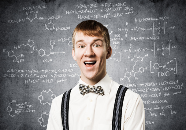 glücklicher Teenager mit breitem Lächeln. emotionaler Rotschopf, der mathematische Berechnungen anstellt. Junge Wissenschaftlerin trägt weißes Hemd, Fliege und Hosenträger auf Kreidetafel mit mathematischen Formeln. - Foto, Bild