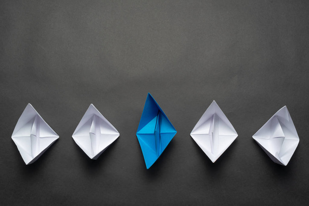 Row of paper ships on black background. Leadership concept with blue paper ship leading among white. Individual motivation and direction. Social marketing layout with copy space. - Foto, imagen