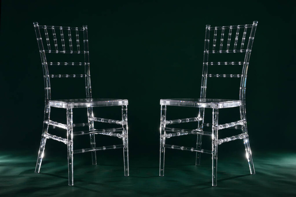 Two transparent plastic chairs on green background in photo studio with light. - Foto, imagen