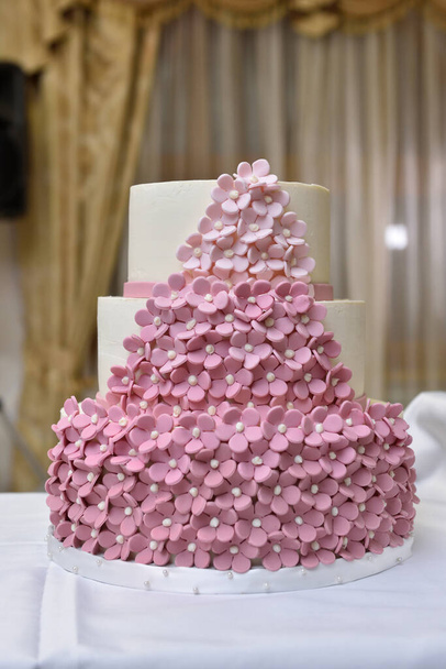 Three-tiered wedding cake decorated with small pink flowers from mastic. - Фото, изображение