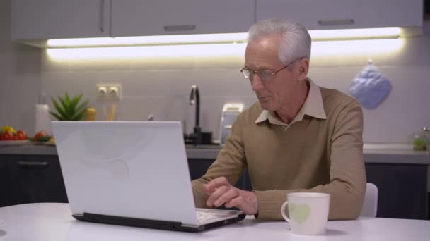 Senior man working on laptop at home table, freelance work, modern technology - Video