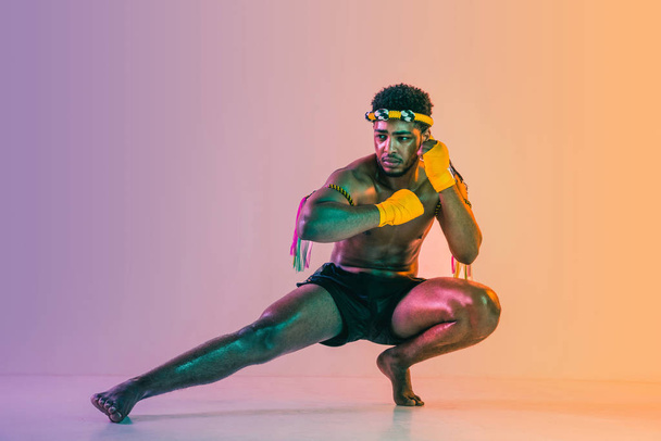 Muay thai. Young man exercising thai boxing on gradient background - Zdjęcie, obraz