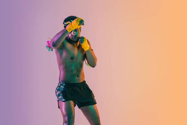 Muay thai. Young man exercising thai boxing on gradient background - Fotoğraf, Görsel