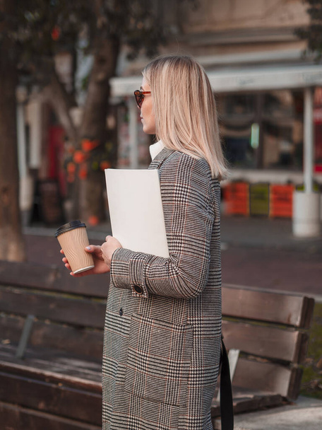 Egy gyönyörű fiatal nő télikabátban, üres borítójú divatmagazinnal az utcán. Függőleges makett a magazinhoz - Fotó, kép