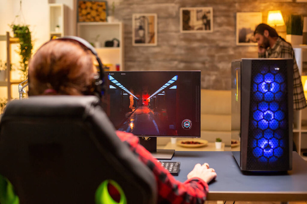Rückansicht einer Spielerin, die spätabends im Wohnzimmer auf einem leistungsstarken Computer-PC spielt - Foto, Bild