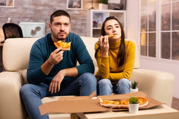 Πανέμορφο νεαρό ζευγάρι τρώει πίτσα ενώ βλέπει τηλεόραση - Φωτογραφία, εικόνα