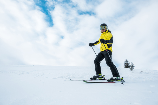 athletic man in helmet and goggles skiing on slope in wintertime - Photo, Image
