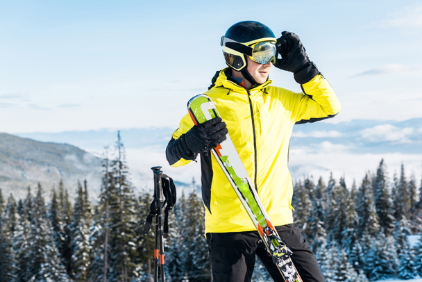skier touching goggles and holding ski sticks against blue sky - Photo, Image