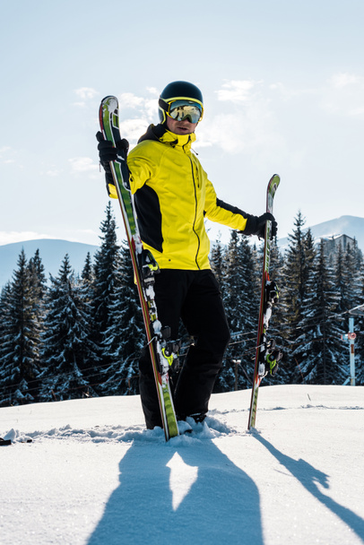 skier holding skis and standing against blue sky in mountains - Photo, Image