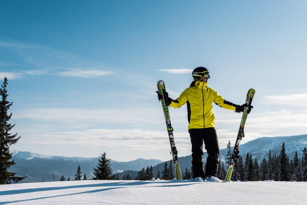 sciatore che tiene gli sci e in piedi contro il cielo in montagna
 - Foto, immagini