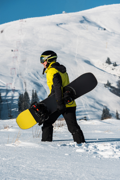 vista laterale dello snowboarder in casco passeggiata in montagna con snowboard
 - Foto, immagini