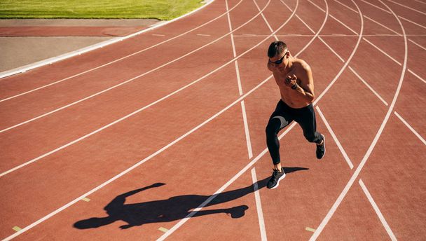 Horizontal image of young man athlete running on a track race in stadium. Athletic male jogging on a sunny day at stadium. People, healthy lifestyle and sport concept - Fotó, kép