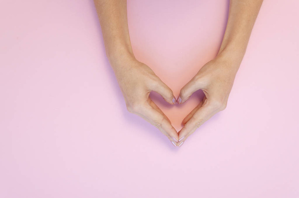 Flat lay fêmea Mãos fazer um gesto em forma de coração no fundo rosa para o dia de S. Valentim
 - Foto, Imagem