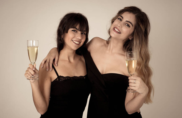 Two beautiful girlfriends having fun celebrating Christmas or New Year eve toasting glasses. Women posing in stylish sexy party dresses drinking champagne. People Friendship and Celebration. - Foto, Imagen