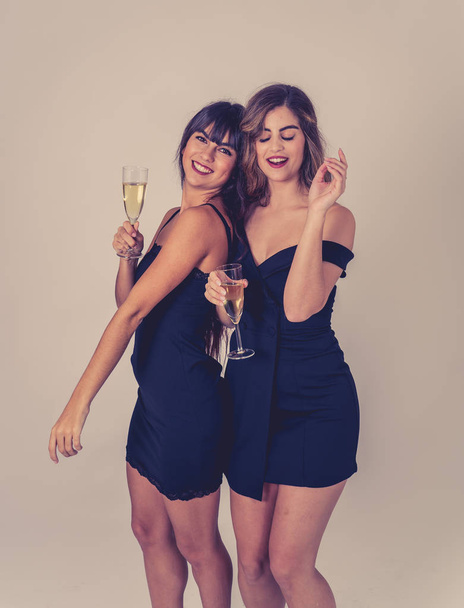 Two beautiful girlfriends having fun celebrating Christmas or New Year eve toasting glasses. Women posing in stylish sexy party dresses drinking champagne. People Friendship and Celebration. - Foto, Imagen