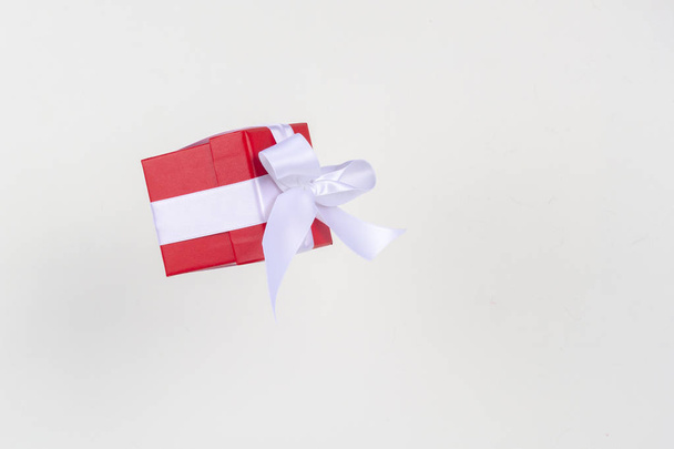 Piros ajándék doboz fehér szatén szalag íj repül fehér háttér. Minimális koncepció a karácsonyi ünnepek, születésnap, Valentin, vásárlás és értékesítés. - Fotó, kép