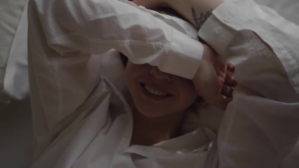Camera moving around face of young Caucasian woman opening face closed with hands. Positive blond woman in white shirt resting on soft bed. Lifestyle, happiness, relaxation. - Filmagem, Vídeo