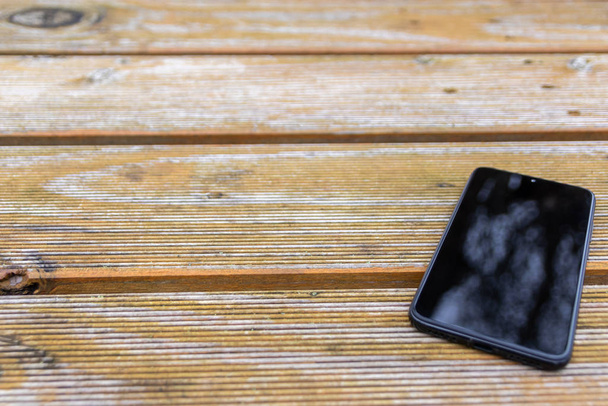 Narušení recepce s černým smartphonem a dotykovým zařízením s čistým reflexním povrchem, které potřebuje robustní pouzdro na mobilní a mobilní zařízení ležící na dřevěném stole - Fotografie, Obrázek