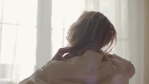 Close-up back view of sensual Caucasian girl touching hair in sunrays. Young woman waking up in the morning at home. Leisure, tranquility, happiness. - Materiał filmowy, wideo