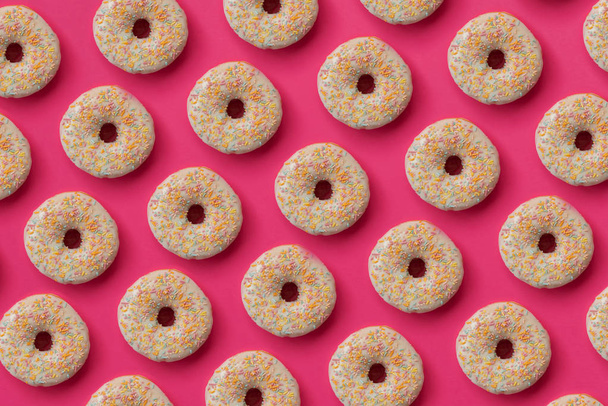 Pattern from glazed donuts decorated colorful sprinkles on pink background. Flat lay. Top view. Unhealthy food - Fotó, kép
