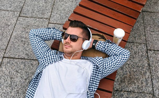 Ο άνθρωπος με τα ακουστικά που βρίσκεται σ ' ένα παγκάκι - Φωτογραφία, εικόνα