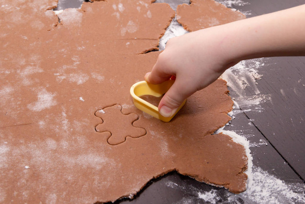 生姜クリスマスクッキーを作るために特別なステンシルを使用して生地から数字をカット.子供たちの手を閉じる。休日の概念のための家、家族の準備 - 写真・画像