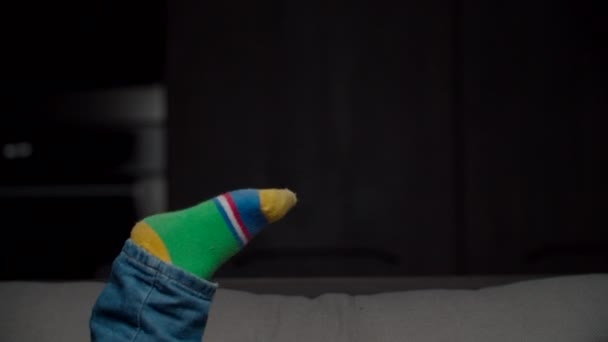 Kids legs in jeans and green socks shaking in the air with dark background. Child laying on sofa with raising up legs in color socks. - Metraje, vídeo
