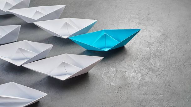 Üzleti vezetés koncepció, Paper Boat, a legfontosabb vélemény Leader, a koncepció a befolyás. Egy kék papírhajó, mint a vezető, amely a fehér hajók felé vezet szürke beton alapon, - Fotó, kép