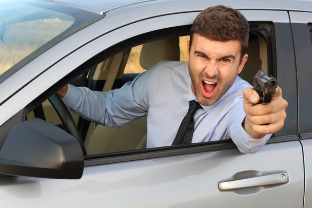 Enojado hombre de negocios gritando mientras conduce el coche y apuntando con arma
 - Foto, imagen