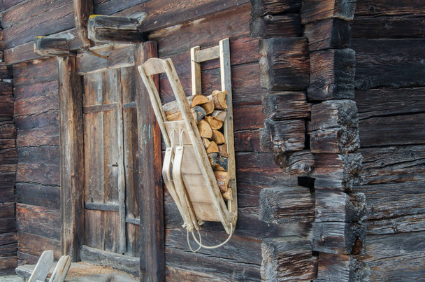 Küçük bir köyde eski ahşap duvarda asılı odun taşıyıcı sırt çantası. - Fotoğraf, Görsel